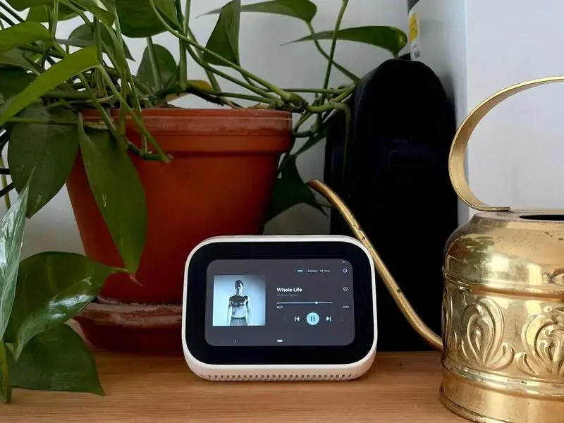Wooden cabinet with a pothos plant in a ceramic pot, a golden water can, and the Xiaomi Smart Clock playing Whole Life by Perfume Genius